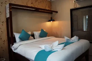 Deluxe room at Tanzanite Boutique Resort near Anjuna Beach, North Goa, with a wooden canopy bed, teal cushions, warm lighting, and elegant interiors.